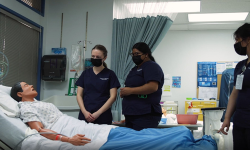 Nursing students stand around medical dummy in bed